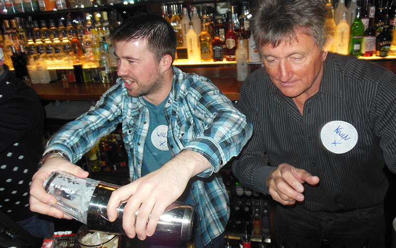 Two men behind a bar, making cocktails