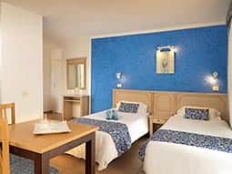 Two single beds in a hotel room, facing a table and chairs