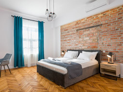 A double bed in a room with an exposed brick wall behind it and large windows at Old City Apartments in Krakow