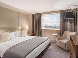 A king size bed in a room with a large window and other seating at Crowne Plaza Glasgow