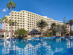 An outside view of a hotel with a large swimming pool and palm trees