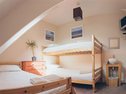 A loft room with a double bed, set of single bunk beds and a chest of drawers at Smarties Surf Lodge in Newquay