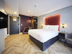 A large bed with a rusty orange headboard and strip led lighting at Roomzzz York