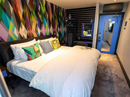 A king bed in a geometric themes room with storage and an en suite at Village Hotel Southampton Eastleigh