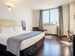A king room with a window that overlooks the city, a desk with a chair and lounge areas at Ilunion Aqua 4 in Valencia
