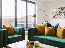 A set of two green velvet sofas with mustard yellow cushions next to large sliding doors that lead onto a balcony at Riverside Apartments in York