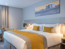 A large double bed with a yellow throw and yellow cushions in a room at Maldron Hotel Smithfield in Dublin