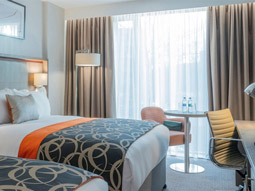 Two twin beds in a room with a large window, a desk with a chair and a table with two armchairs at Clayton Hotel Charlemont in Dublin