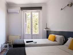 Two single beds in a room with a large window and yellow and grey decor at Roisa Centro Apartments in Madrid
