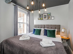 A king bed in a room with a beside table, window and artwork above the bed at Spurriergate York