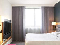 A double bed in a room with a large window and TV at Moxy Glasgow