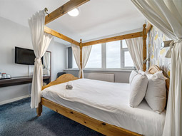 A large 4 poster bed in a room with a desk and TV at Bluewater Hotel