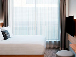 A double bed facing a TV with a large window beside it at Moxy