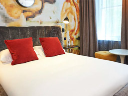 A bed with red cushions and a patterned wall behind it at Malmaison in London 