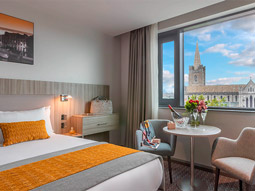 A double bed in a room with a coffee table area and a view of the city at Maldron Kevin Street