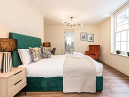 A bedroom in Rodney Street Townhouse with a double bed that has silver decorative cushions on it and a red chair in the corner 