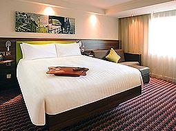 A white double bed with a city skyline picture above the bed, with a brown leather sofa to one side of the bed