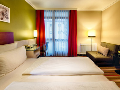 Two single white beds in a green hotel room, facing a TV on a desk