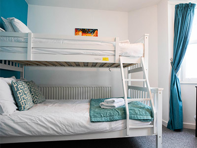 A double bed in a red bedroom, facing a table and TV on the wall