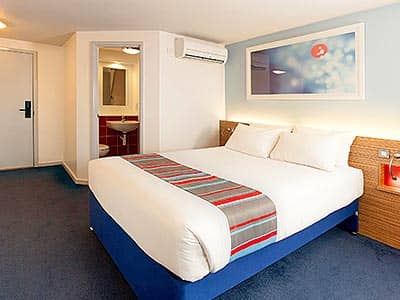 A double bed in a hotel room, with an en-suite visible in the background