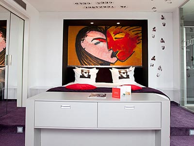 A double bed in a hotel room, set against a wall with a mural hanging above
