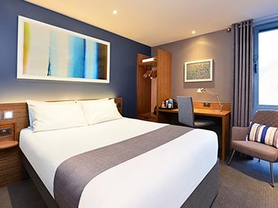 A large white bed with a grey runner laid across it 