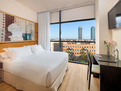A double bed in a room with a large window that overlooks the city at H10 Marina in Barcelona