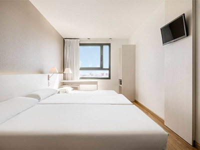 A plain room with two double beds, a TV and desk space with a view of the city at Ilunion Valencia 3