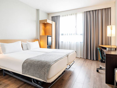 A twin room with a bedside TV, a desk and chair and storage at Ilunion Valencia 4