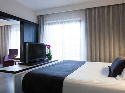 An open plan room with a double bed, a TV and a living area with cushioned armchairs at Dimar Hotel in Valencia