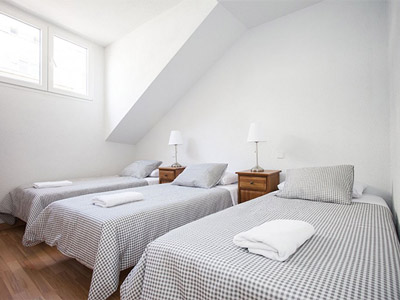 Three beds in a loft room with small windows and bedside tables with lamps on at Fuencarral Apartments in Madrid