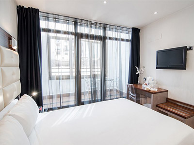 A king bed in a room with a tv on the wall in front of it and a large set of glass sliding doors that lead onto a balcony at Petit Palace Cliper Gran Via Hotel in Madrid 