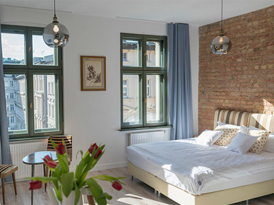 A large bed in a spacious room with two long windows at Provenir Home Apartments