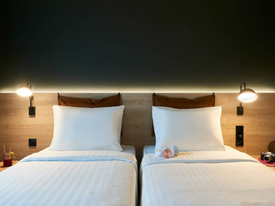 Two single beds against a headboard with warm lighting and a dark wall at Moxy Chester