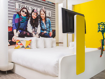 A king bed with a TV on the end of it in a yellow themed room at The Corner Hotel