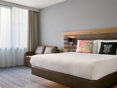 A king bed in a room with a leather sofa and large windows at Moxy Hotel