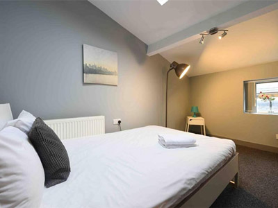 A double bed with white sheets on in a room with warm lighting at Back Turner Townhouse