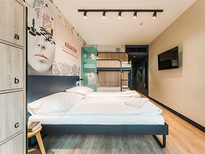 Two single beds and a set of bunkbeds in a room with a TV on the wall at Meininger Krakow Centrum