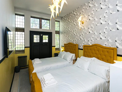 Two double beds in a room with lots of windows and warm lighting at All Saints Rooms