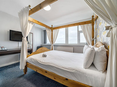 A large 4 poster bed in a room with a desk and TV at Bluewater Hotel