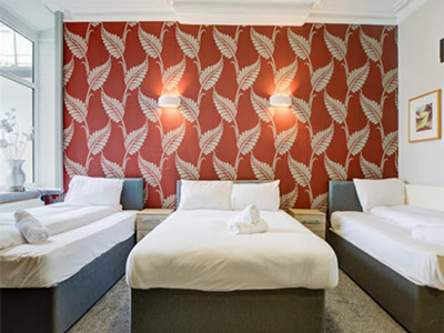 Two single beds with a double bed between them, against a patterned wall at The Sandringham Apartment