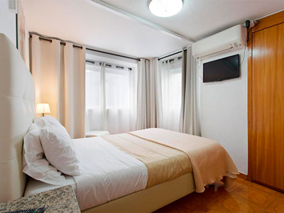 A double bed in a room with large windows and a TV on the wall at Braganca Oporto Hotel