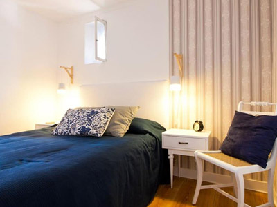 A double bed in a room with a bedside table and chair at Lisbon Sant'Anna Apartments