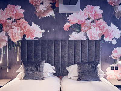 A hotel bedroom with two single beds and a bold wallpaper with big bunches of pink flowers 