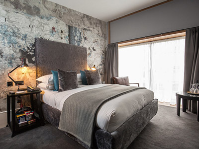 A hotel bedroom with a double bed and map themed wallpaper 