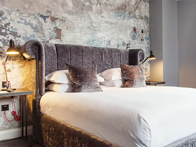 A stylish looking hotel room with map-themed wallpaper a double bed that has a grand-looking headboard 