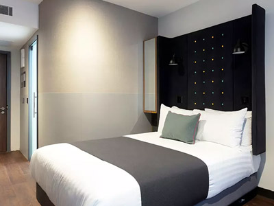 A modern hotel room with a double bed that has a very high black headboard 