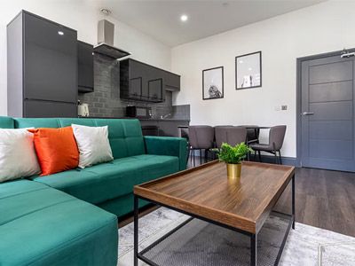 An open plan living and dining area that has a green corner sofa and a big wooden coffee table 