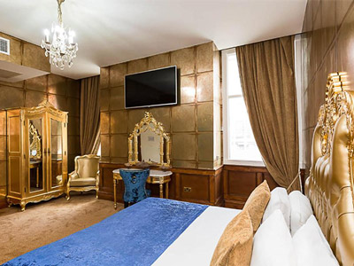 A grand looking bedroom at the Dixie Dean hotel with a large bed, gold coloured wardrobe and a wall mounted flatscreen TV 