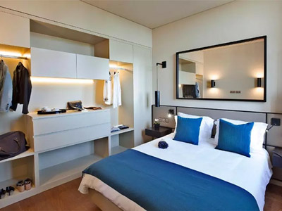 A bedroom at Lisbon Apartments 8 Building which looks smart with a double bed, large mirror above the bed and white clothing storage 